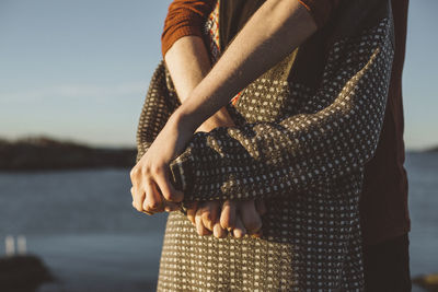 Midsection of woman holding umbrella standing at shore