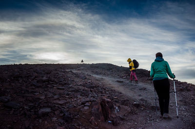 Rear view of people walking on mountain against sky