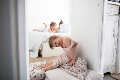 Funny toddler girl next to sisters, playing on laptop on bed. concept happy childhood and siblings, 