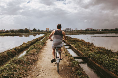 Rear view of man riding bicycle on water against sky