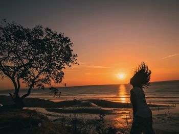 Silhouette woman standing on beach against sky during sunset