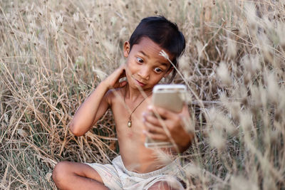 Portrait of boy photographing through smart phone in field