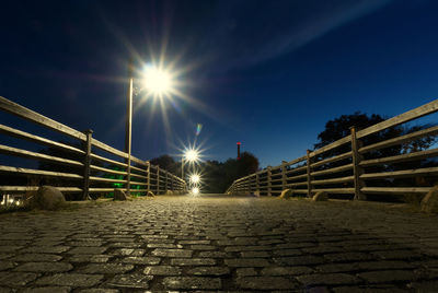 Illuminated footpath by street against blue sky