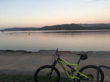 Bicycle by lake against sky during sunset