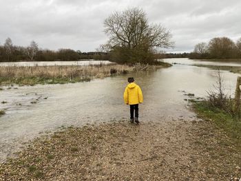 Rear view of boy standing on flooded riverbank