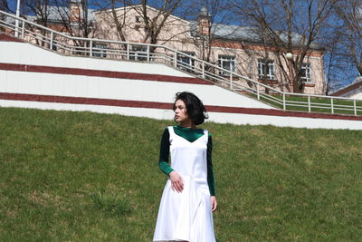 Young woman standing on field against building