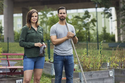 Portrait of mid adult couple with gardening tools at urban garden