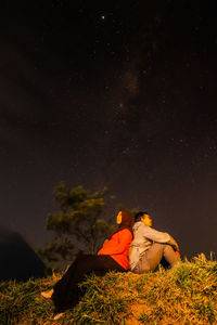 Rear view of couple sitting on field against sky at night