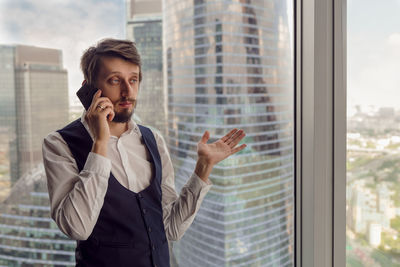 Businessman with beard is talking
on the phone in a skyscraper apartment in the afternoon in summer