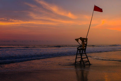 Silhouette lifeguard hut on beach against sky during sunset