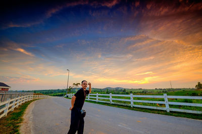 Man standing on road against sky during sunset