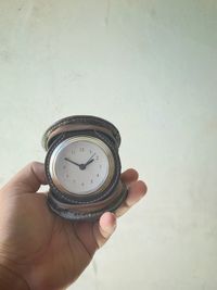 Close-up of hand holding clock against wall