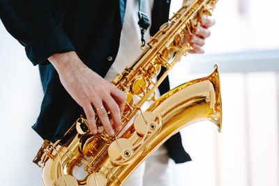 Crop male musician playing saxophone while standing on white background and looking away