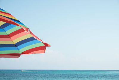 Close-up of multi colored umbrella by sea against clear sky