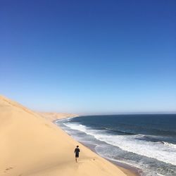 High angle view of man running at beach against clear blue sky