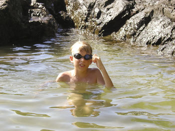 Shirtless boy wearing swimming goggles in lake