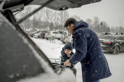 Father with son sitting in shopping cart at snowy parking lot