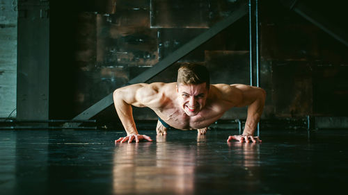 Portrait of shirtless muscular man doing push-ups at home