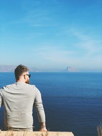 Rear view of man by sea against blue sky