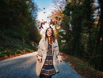 Portrait of smiling young woman by road against trees