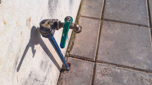 High angle view of faucet on footpath by wall