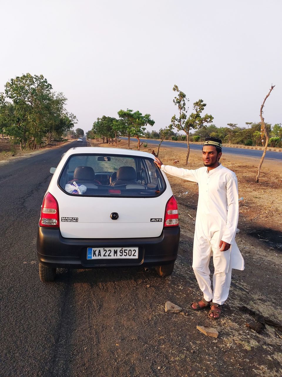 MAN STANDING BY CAR AGAINST SKY