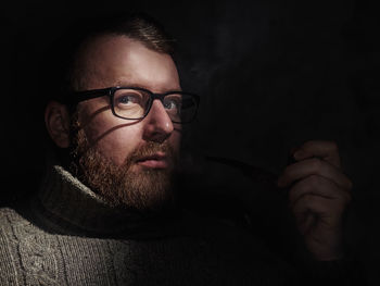 Portrait of mature man smoking while sitting in darkroom