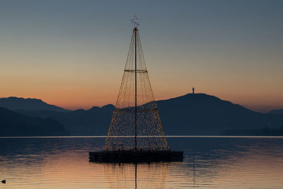 Illuminated christmas tree amidst lake against sky during sunset