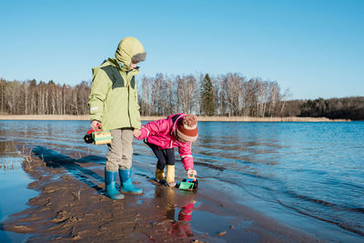 Siblings holding hands at the beach whilst playing with toys