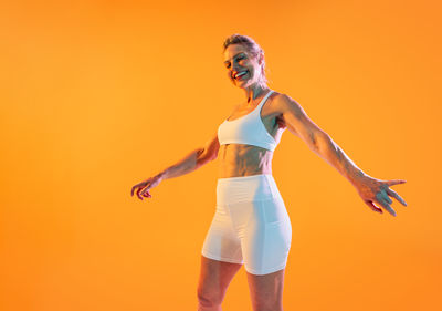 Rear view of woman with arms raised standing against yellow background