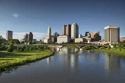 Bridge over river by buildings in city against blue sky