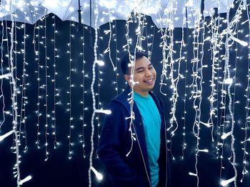 Smiling young man standing amidst illuminated decoration