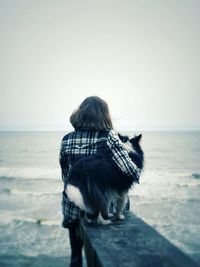 Rear view of woman sitting with dog at beach against clear sky