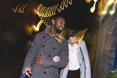 Happy couple in trench coats walking at night