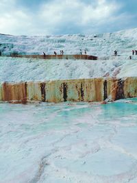 People on travertine pool against sky