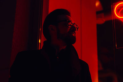 Young man wearing sunglasses standing in illuminated club