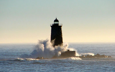 Lighthouse amidst sea and buildings against clear sky