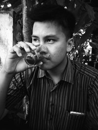 Young man drinking juice in glass against trees