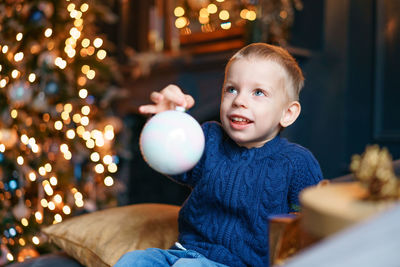 Happy little boy sitting on sofa with christmas tree decoration in cozy living