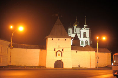 Illuminated street amidst buildings against sky at night