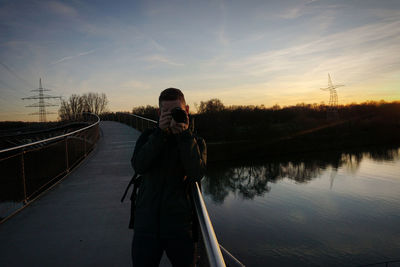 Man mann kamera camera reflection see lake sunset sonnenuntergang bridge brücke tree baum reporter 