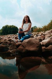 Young woman sitting on rock against sky