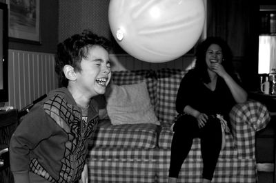 Cheerful mother looking at son playing with balloon at home