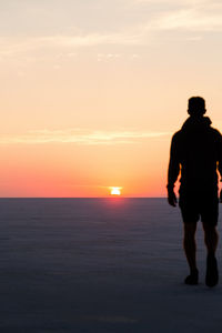 Silhouette man standing on beach against sky during sunset