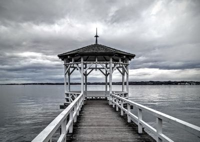 Pier leading to sea against cloudy sky