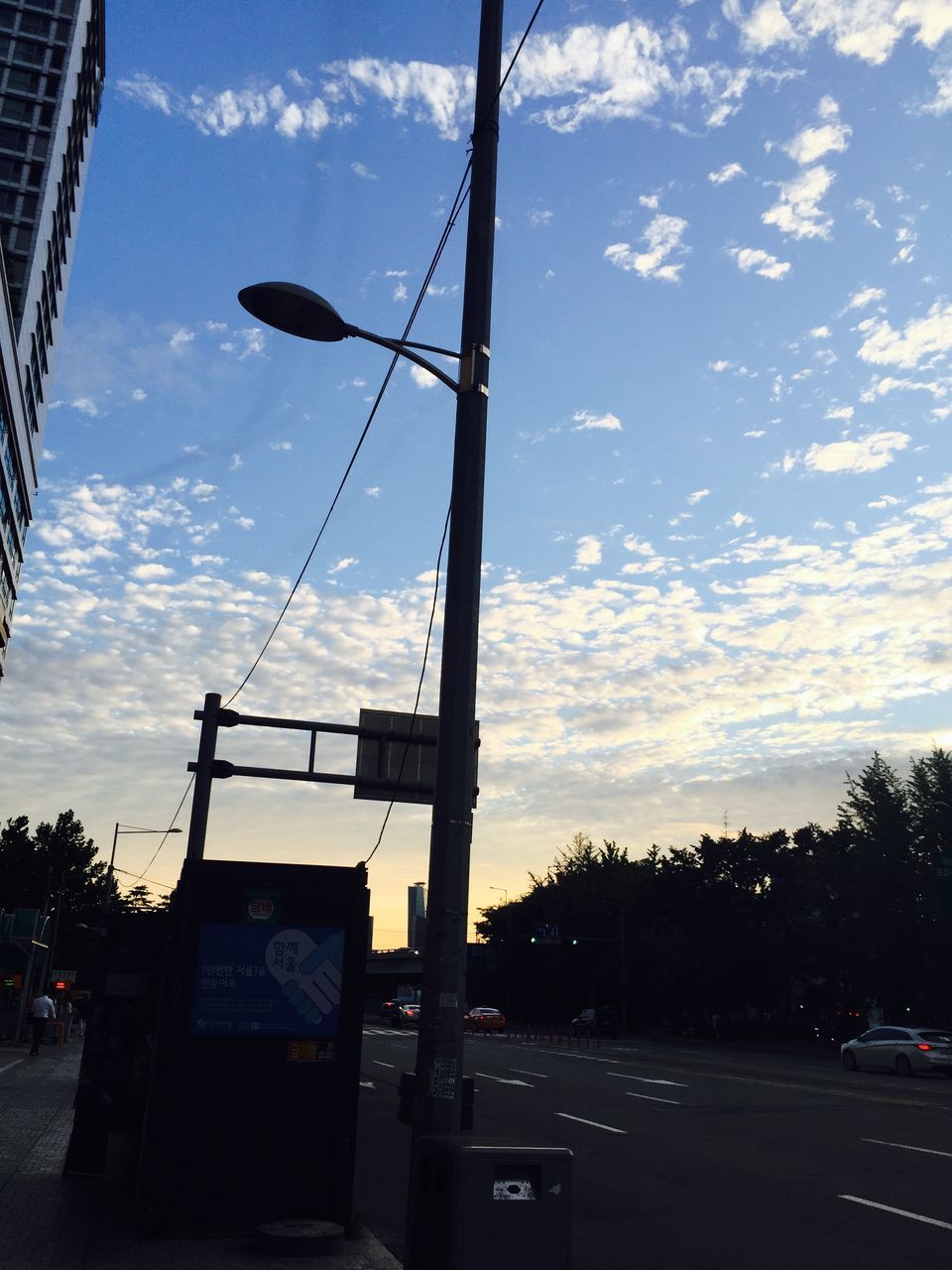 sky, transportation, low angle view, cloud - sky, built structure, architecture, building exterior, road, cloud, street, electricity pylon, pole, mode of transport, car, cloudy, power line, communication, land vehicle, tree, no people