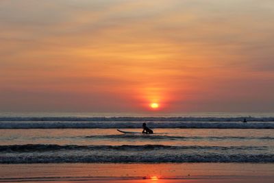 Person surfing in sea against cloudy sky during sunset at kuta