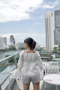 Young woman standing on railing against cityscape