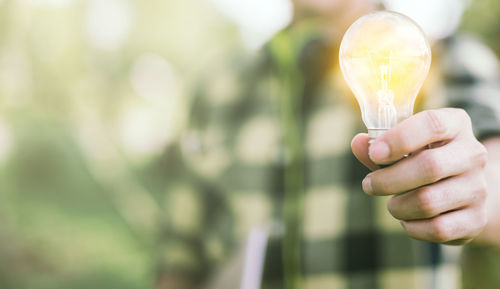 Midsection of man holding illuminated light bulb