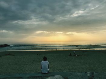 Rear view of women standing on beach against sky during sunset